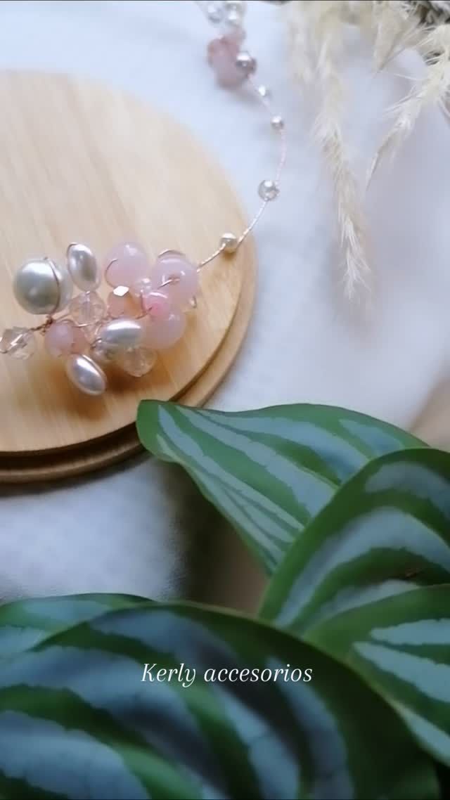 Pinza para el pelo de cuentas en tonos pastel sobre una superficie de madera, con hojas verdes y flores blancas