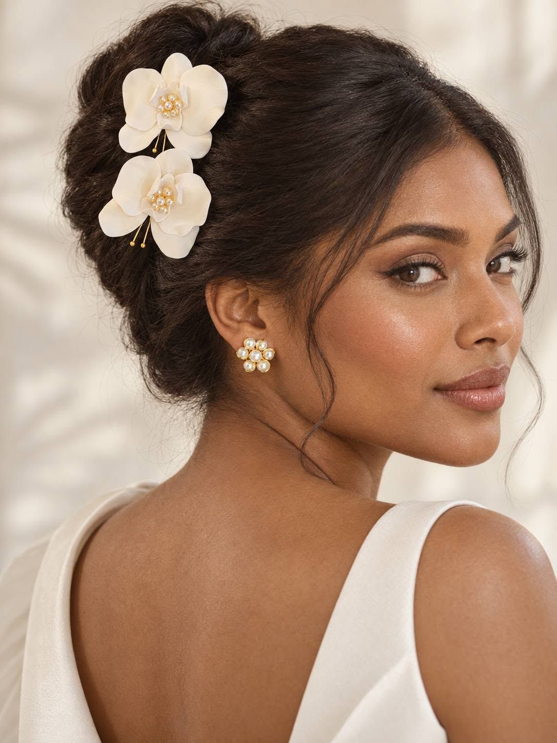 Mujer con un elegante recogido, un adorno floral blanco en el pelo y un vestido blanco, mirando por encima del hombro.