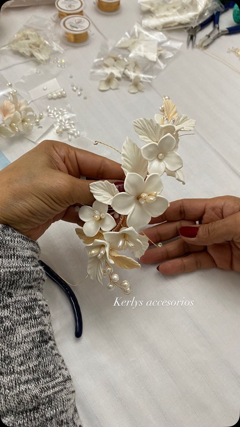 Manos colocando una guirnalda floral blanca sobre una mesa de manualidades, con pétalos y materiales esparcidos