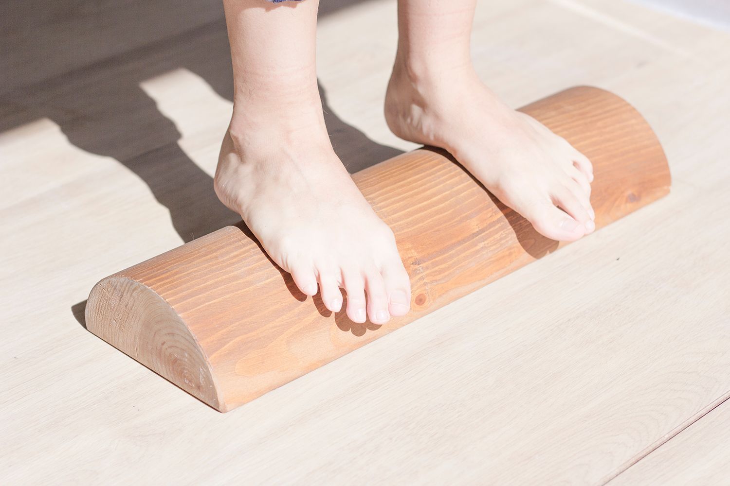 Pies apoyados sobre un rodillo de madera, probablemente para hacer ejercicio o terapia, sobre un piso de madera clara.