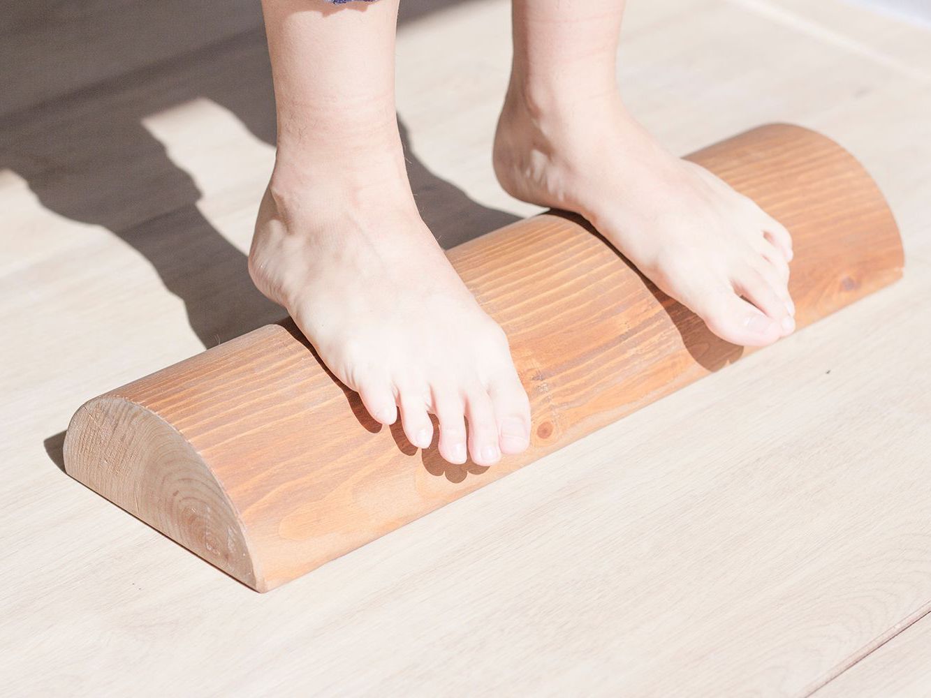 Pies descalzos sobre un rodillo de madera, probablemente para hacer ejercicio o masaje, sobre un piso de madera clara.