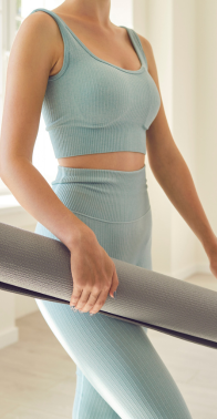 Mujer vestida con ropa deportiva azul sosteniendo una colchoneta de yoga gris en el interior.