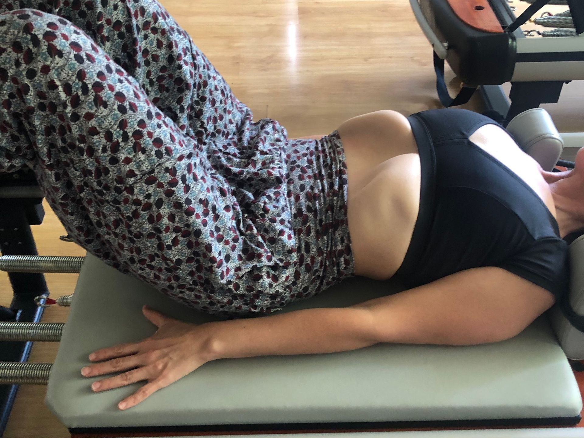 Persona acostada boca arriba, levantando las caderas, realizando un ejercicio de Pilates en una máquina, en un estudio de fitness.