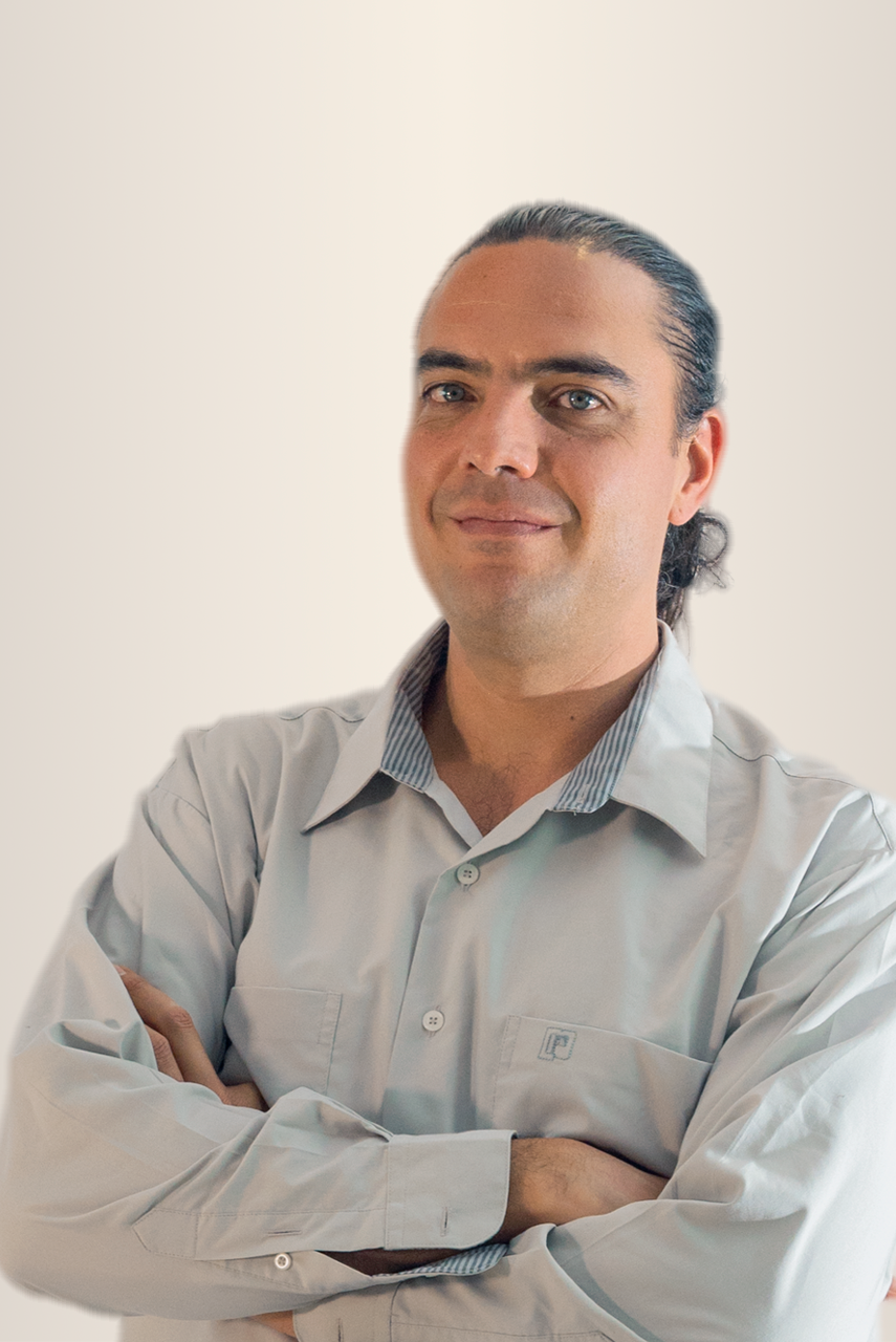 Hombre con camisa azul, brazos cruzados, sonriendo, sobre un fondo neutro.