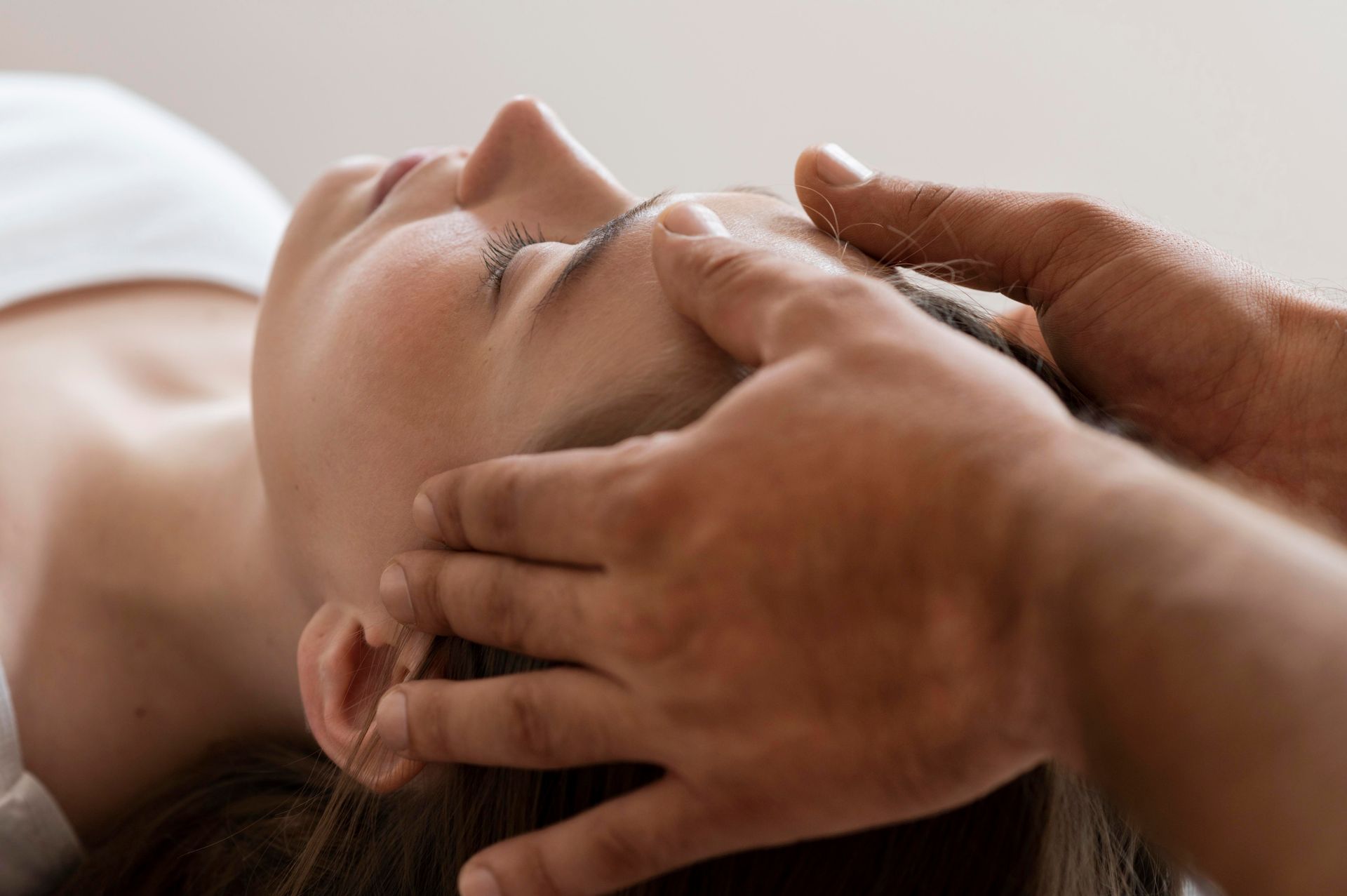 Persona recibiendo un masaje facial; manos en la cabeza y la cara, ojos cerrados, descansando.