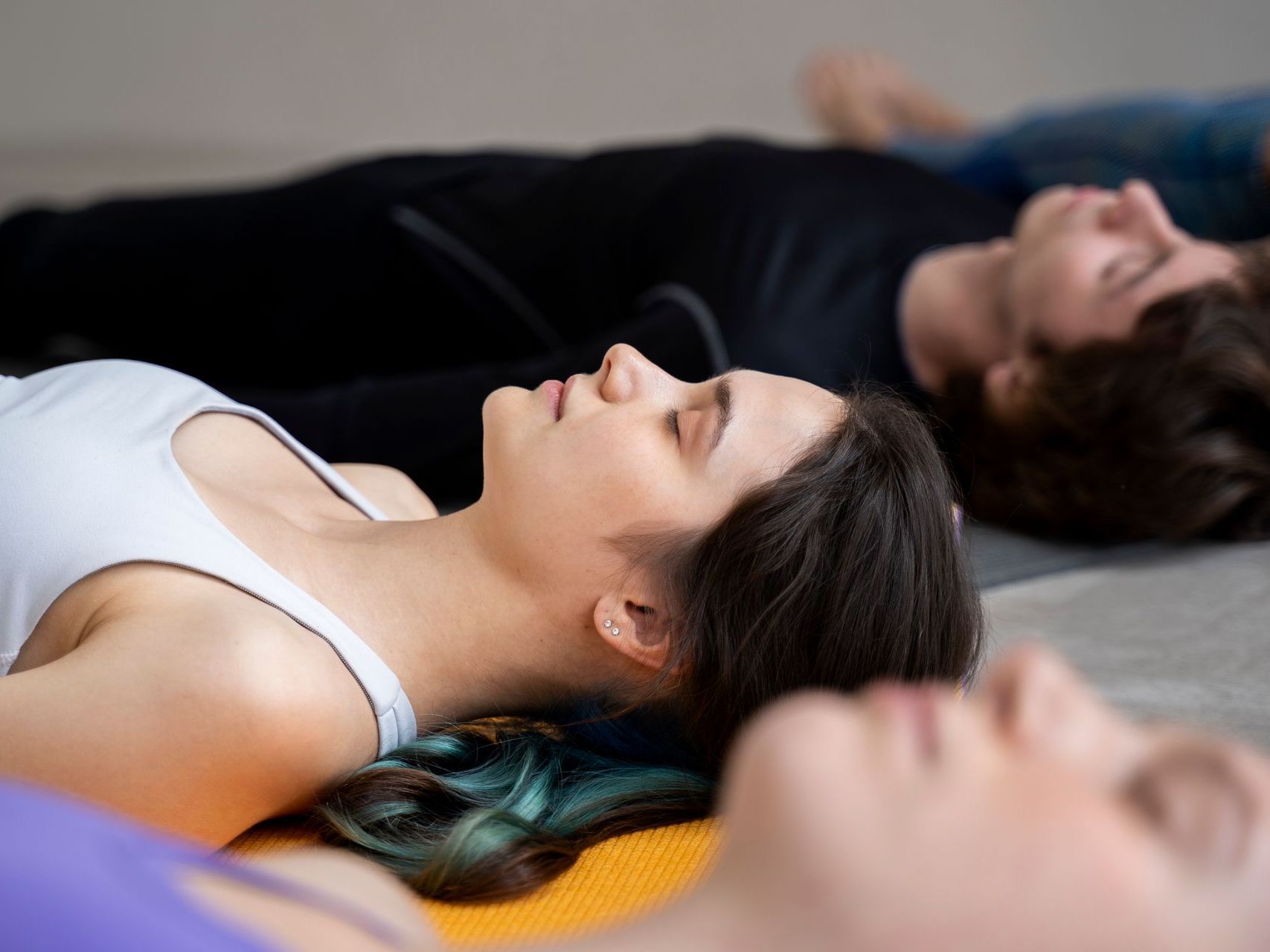 Personas acostadas durante una sesión de yoga o meditación; en el interior con colchonetas de colores neutros.