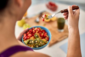 Mujer sosteniendo un tenedor con fruta, a punto de comer de un tazón de frutas mixtas.