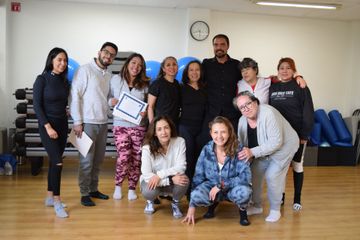 Grupo de personas en el gimnasio; algunas con certificado. Suelo de madera y globos azules de fondo.