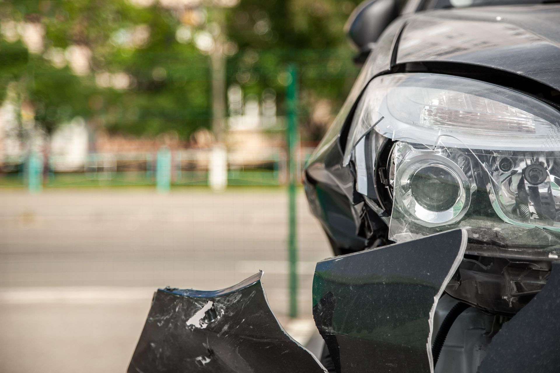 Front-right view of a black car with a damaged bumper and headlight after a collision.