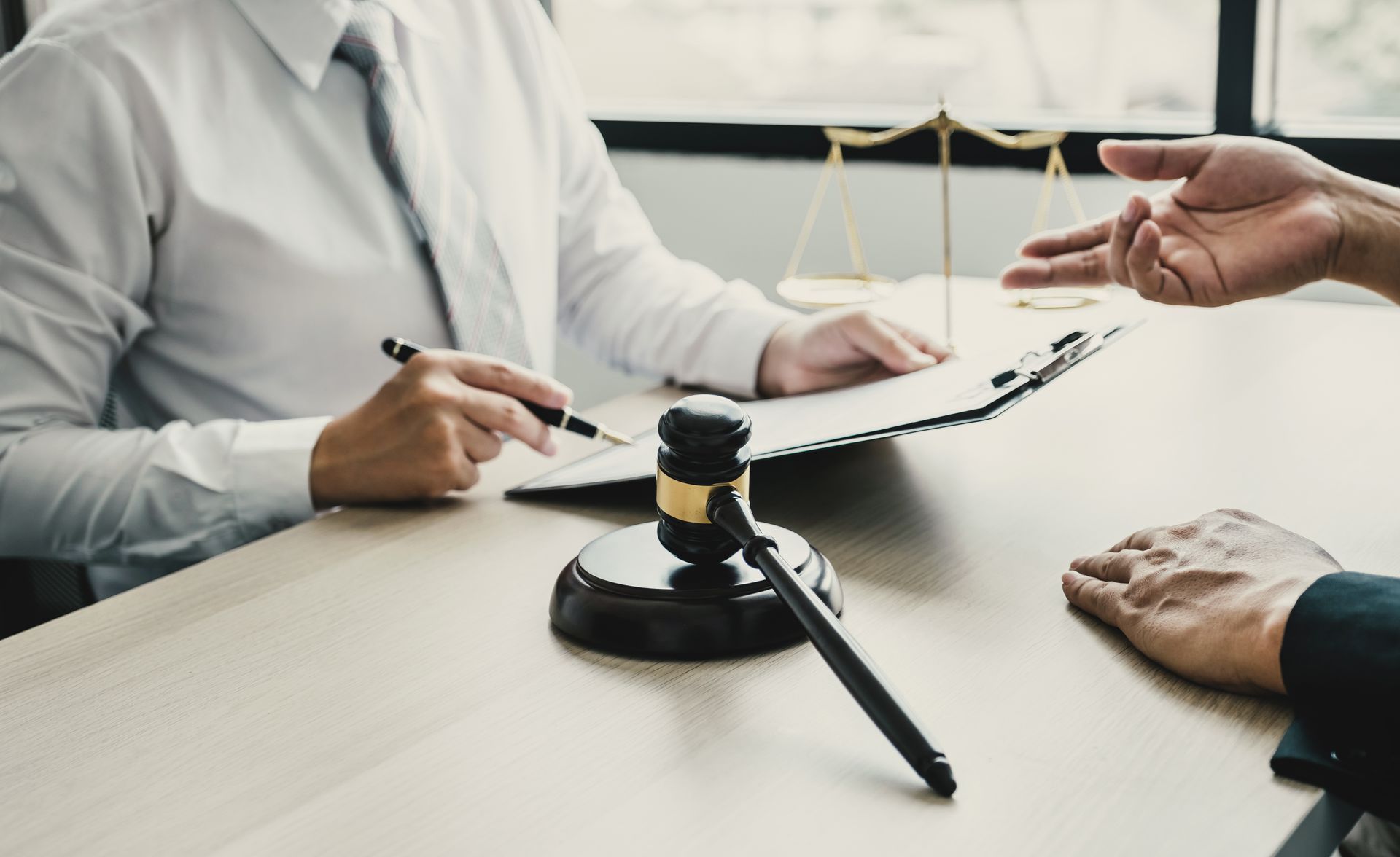 Lawyer and client at table with documents, gavel, and scales of justice.