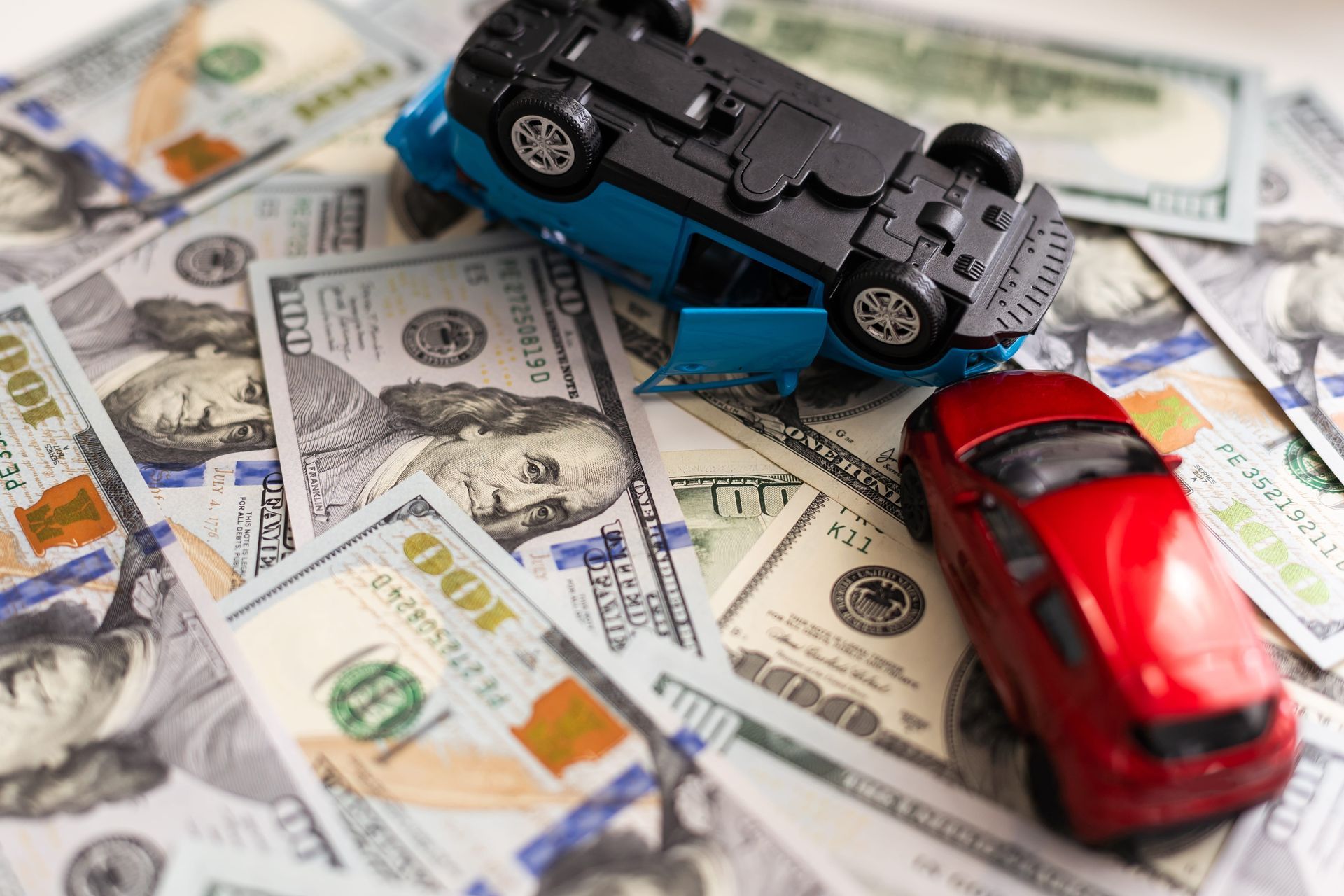 Two toy cars on U.S. dollar bills, one black overturned and one red upright