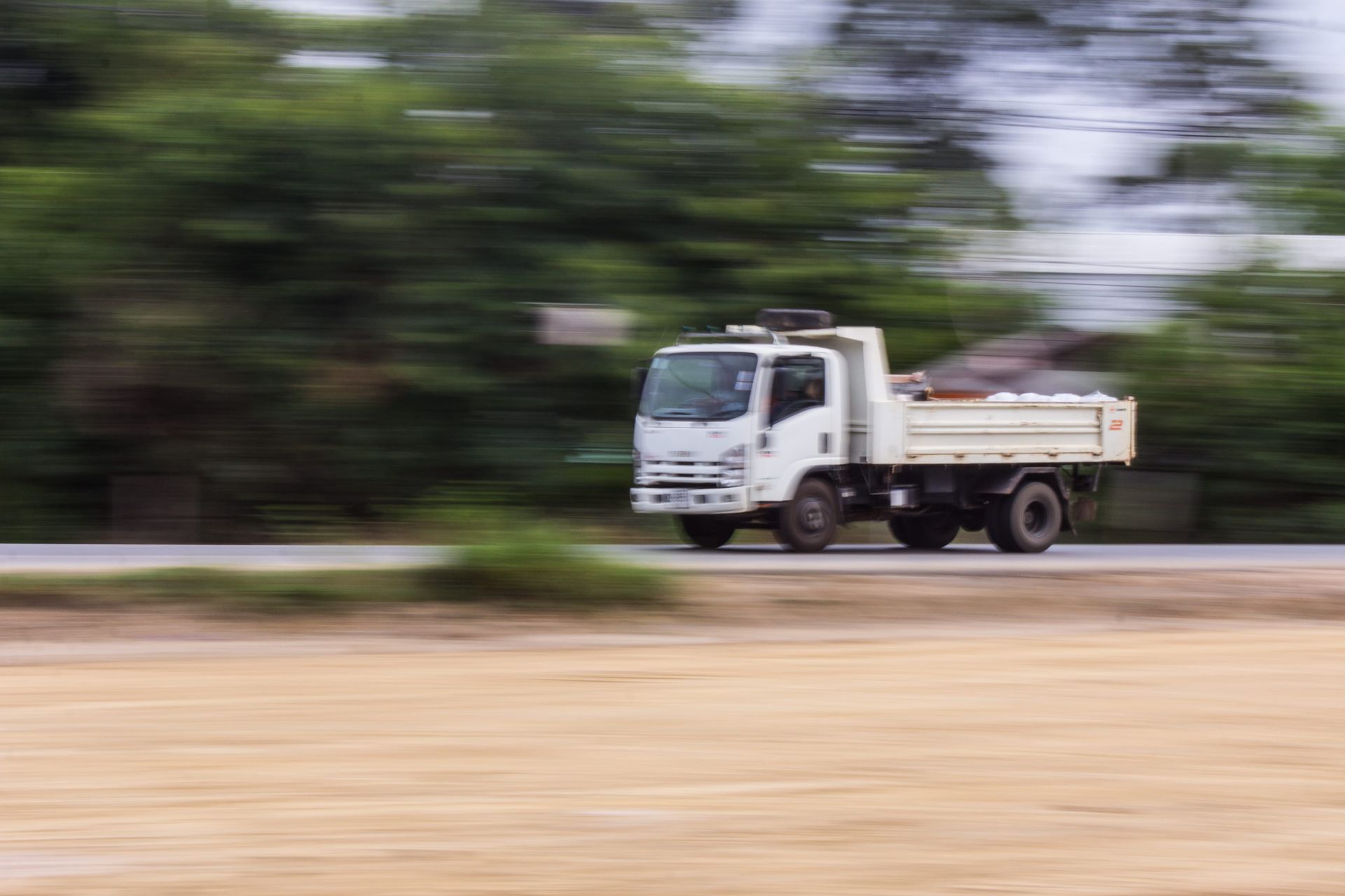 White dump truck driving fast on a road, with motion blur and trees in the background