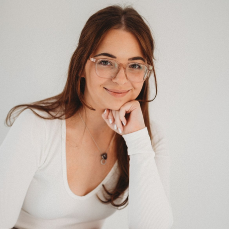 Woman in glasses seated indoors, smiling while looking at a phone.
