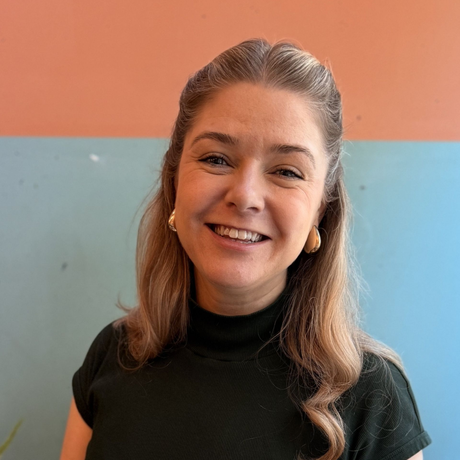Smiling woman in a dark green top against a peach and light blue wall