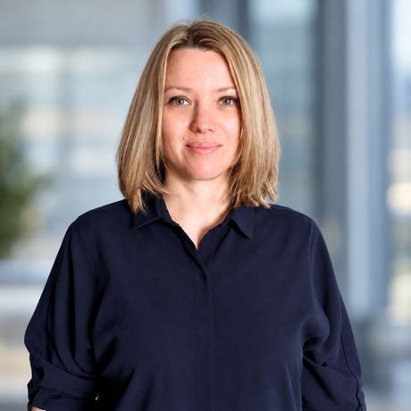 Woman in a navy shirt standing against a blurred office background.