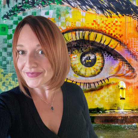 Woman in black top posing before a colorful mural of a large yellow eye
