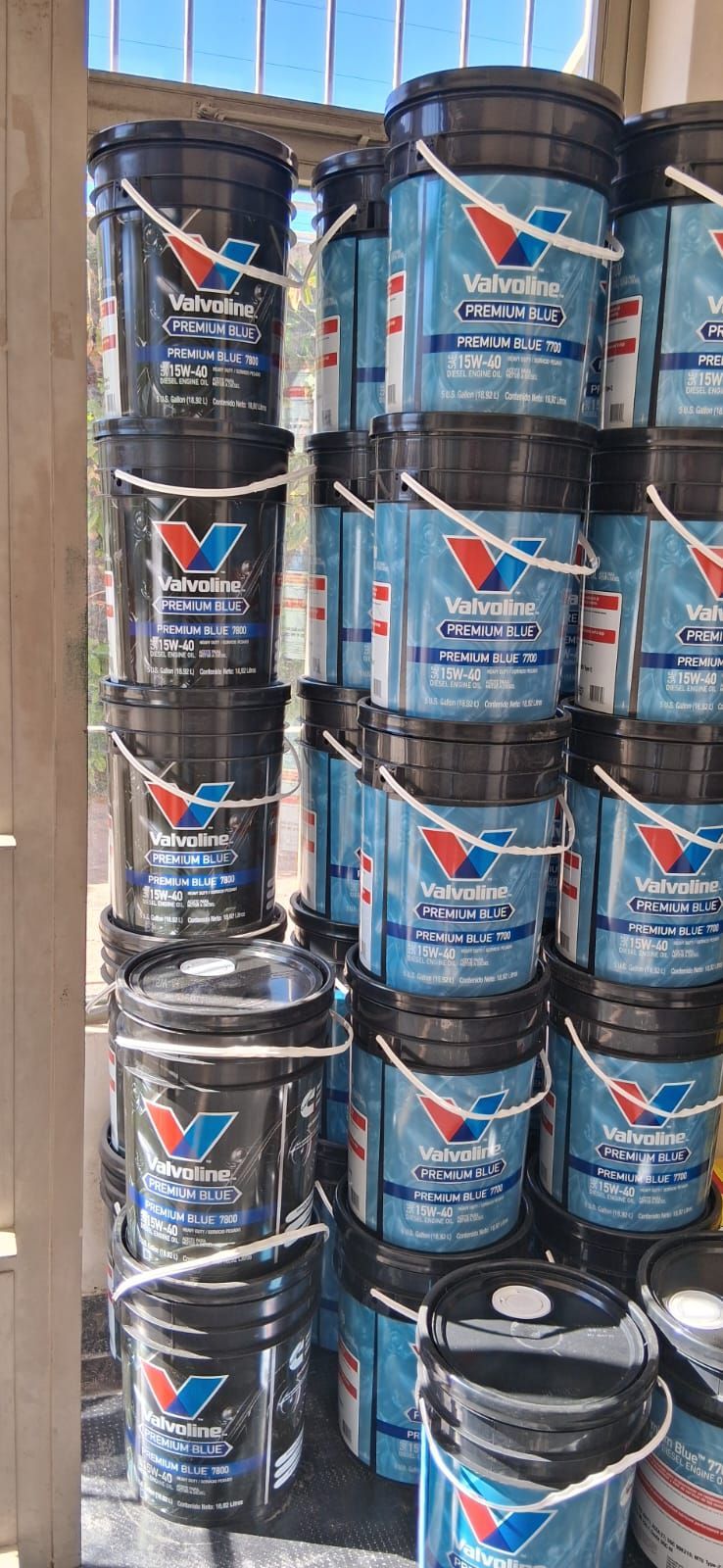 Pilas de cubos de pintura negra con etiquetas azules dispuestas en los estantes del almacén.