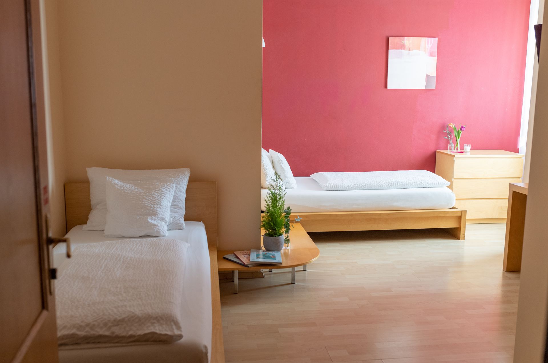Zimmer Hotel Maria, zwei Einzelbetten in einem Verwinkelten Raum. Eine Wand ist Rot gestrichen.