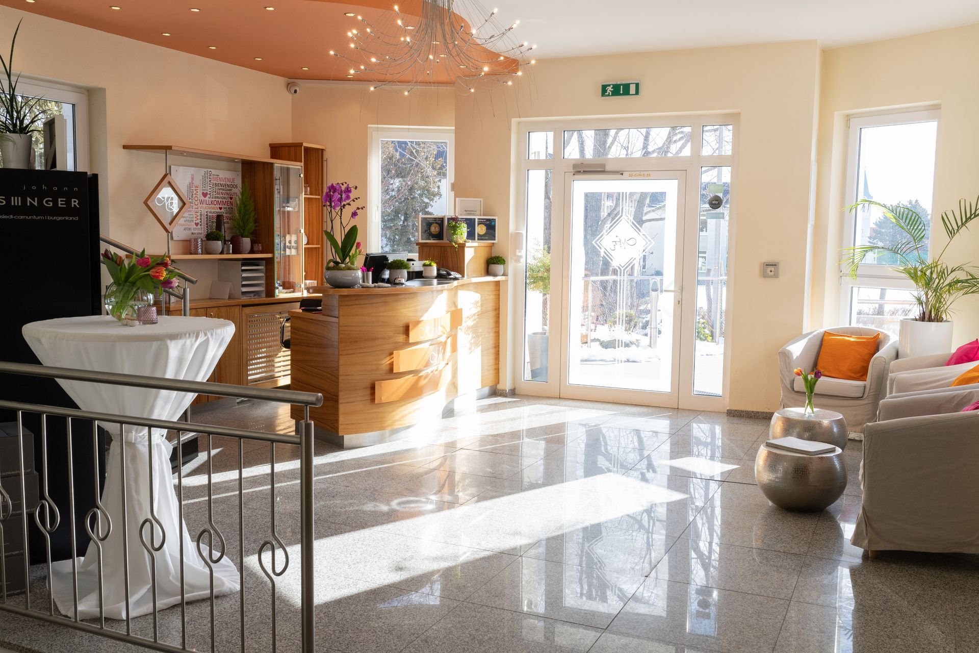 Eingangsbereich Hotel Maria. Warme und sonnige Stimmung, die Wände sind hellgelb, die Rezeption aus warmen Holz.