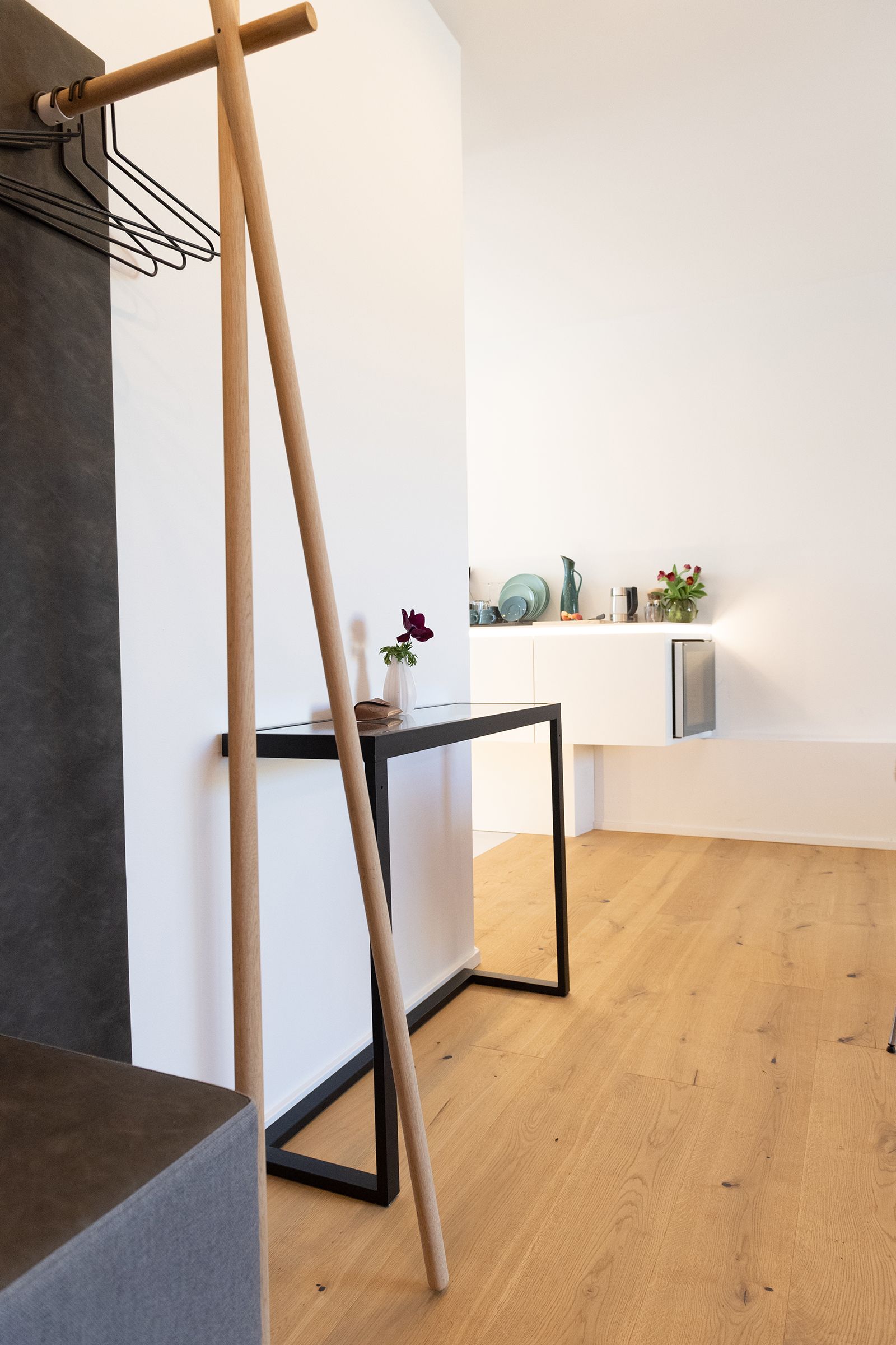 Ein Teil der weißen Küchenzeile und den darauf platzierten Pflanzen ist zu sehen. Davor ist eine graue Garderobe mit Holzakzenten. 