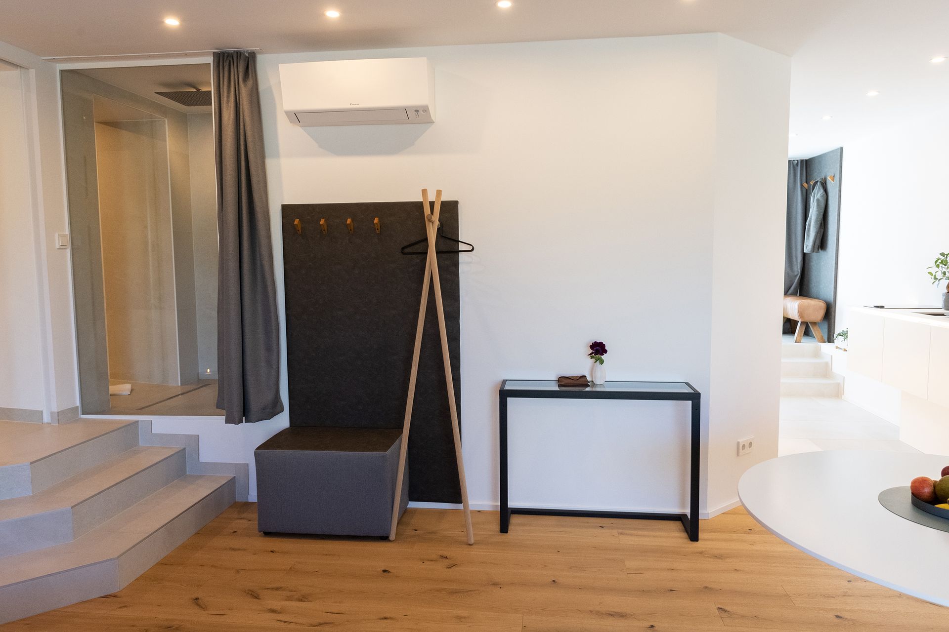 Frontalansicht auf die Graue Garderobe mit Holzakzenten an einer weißen Wand mit LED Spots Beleuchtung an der Decke.