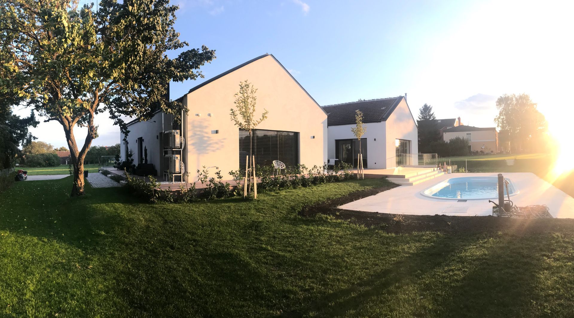 Außenansicht der Holzterrassen von Apartment 6, 7 und 8. Die großen Fenstertüren von Appartment 8 stehen im Fokus. Jede Terrasse hat einen grauen Stoffsessel und Pflanzen. Der Rasen ist gepflegt und grün. Ein Baum ragt von der Seite in das Bild hinein.