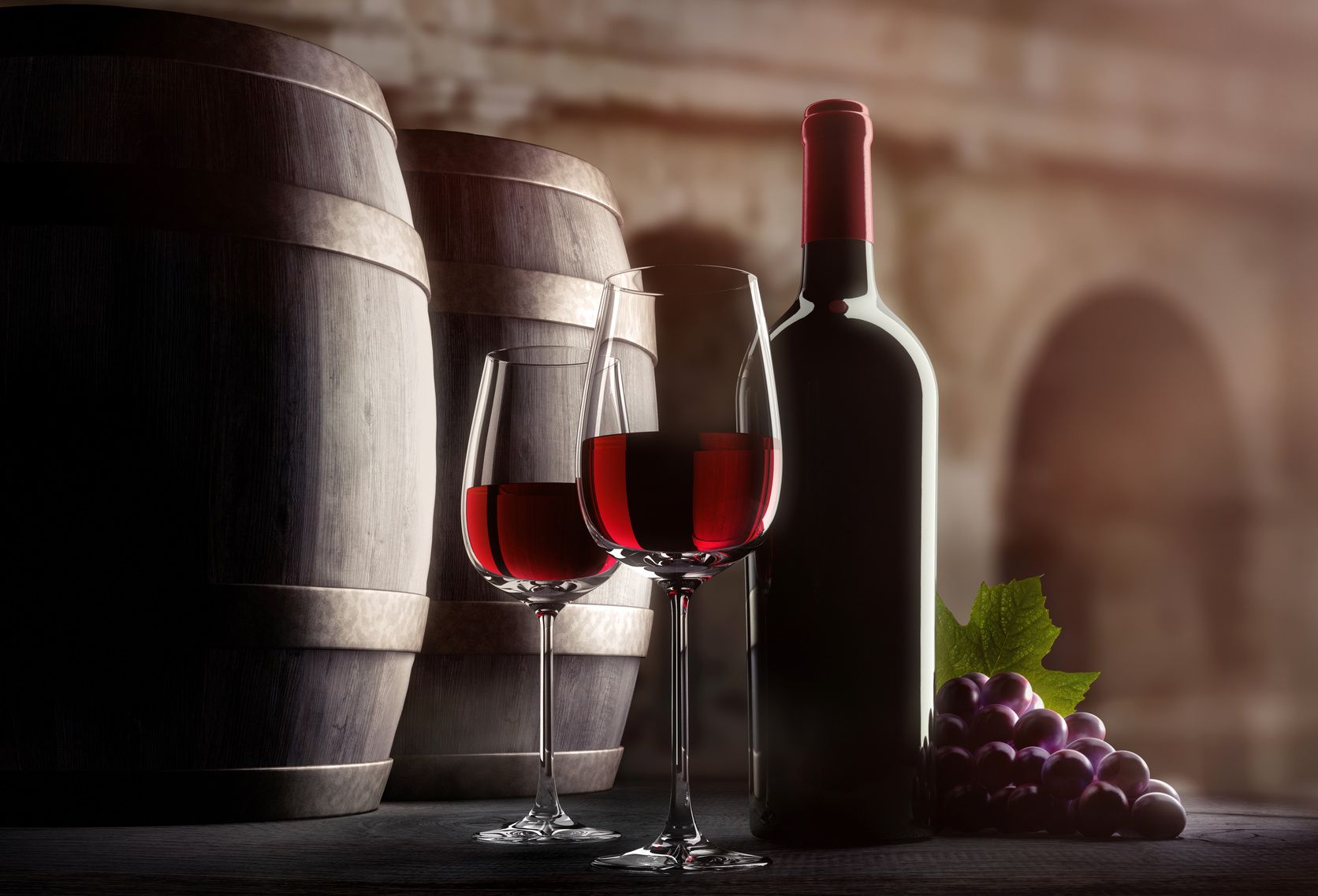 Rotwein im Weinglas und eine Rotweinflasche daneben. Weinfässer dahinter.