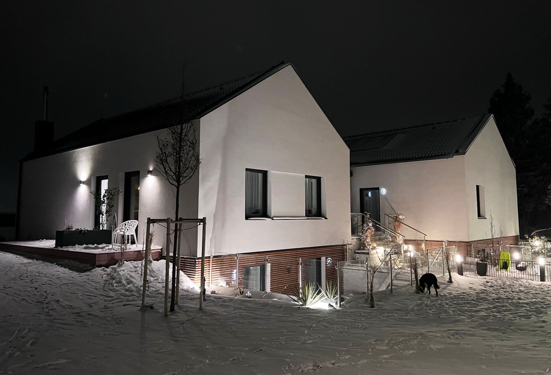 Außenansicht frontal bei Nacht. Großes weißes haus mit Holzelementen. ein Pflasterstein Weg führt zu Appartment 1, 2, 3, 6 und ist beleuchtet.
Der angrenzende Rasen ist mit Schnee bedeckt.