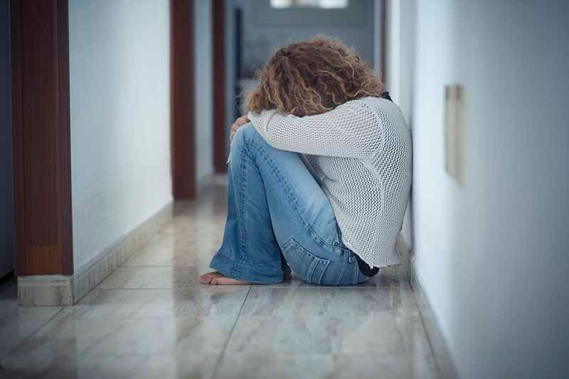Eine junge Frau sitzt im Flur auf dem Boden. Sie hat den Kopf in den Armen verborgen. Stockbild