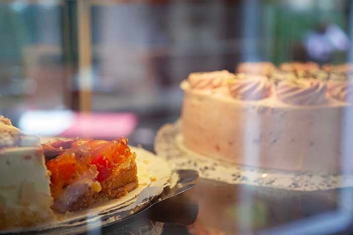 Zwei Kuchen in einer Glasvitrine: einer mit leuchtend orangefarbenen Früchten verziert, der andere mit rosa Zuckerguss.
