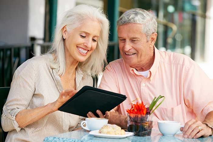 Senioren-Paar blickt gemeinsam auf ein Tablet, beide lächeln entspannt. Stockbild