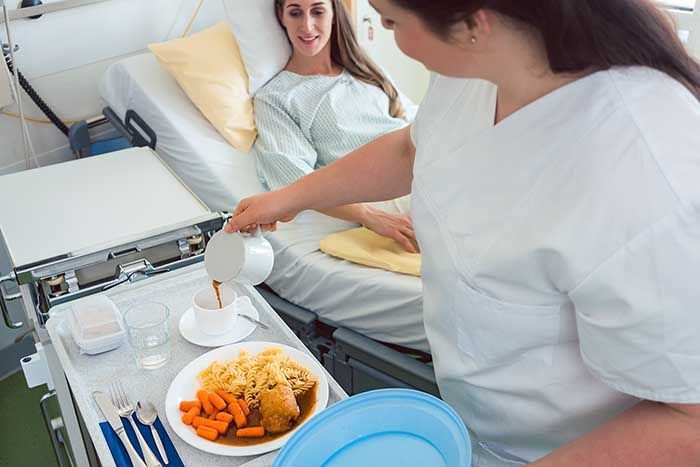 Eine ambulante Pflegekraft serviert am Krankenbett eine warme Mahlzeit und schenkt Café ein. Stockbild