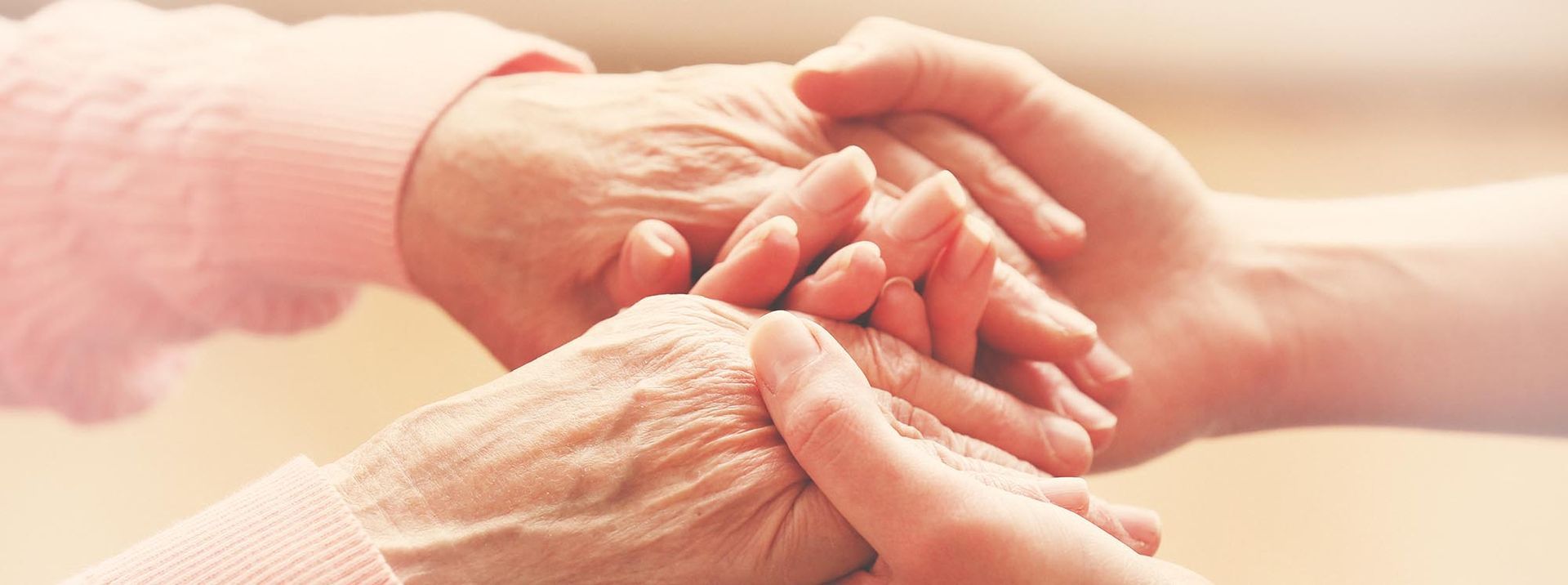 Hände in mildem Licht. Die beiden Hände einer Seniorin und einer jungen Frau. Die junge Frau umfasst die Hände der Seniorin von unten und gibt Halt. Stockfoto
