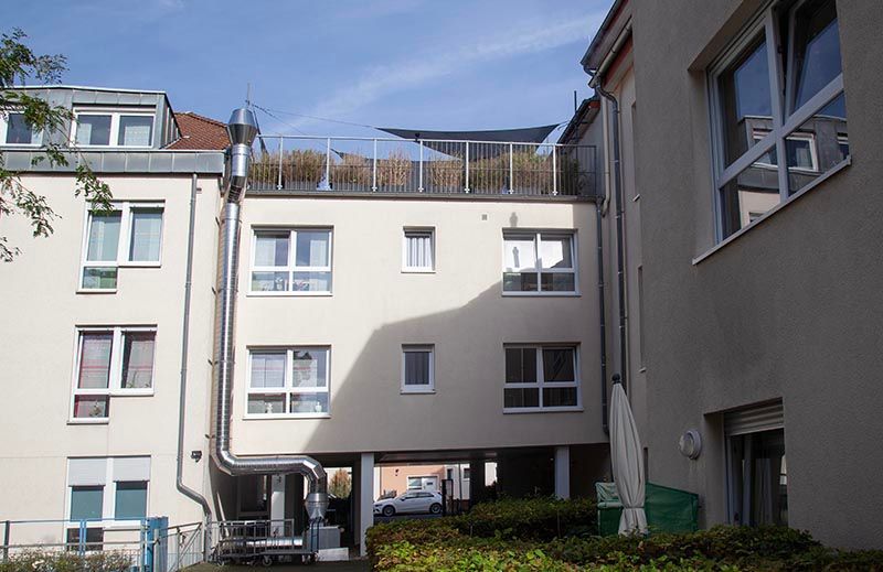 Ein cremefarbenes Gebäudeäußeres mit Dachterrasse, Metallgeländer und einem außenliegenden Metalllüftungsrohr.
