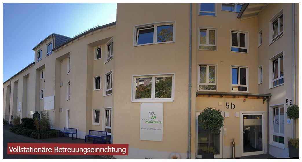 Ein mehrstöckiges, beigefarbenes Wohngebäude mit einem zentralen Eingang, der mit „2b“ gekennzeichnet ist, und einem kleinen Topfbaum.