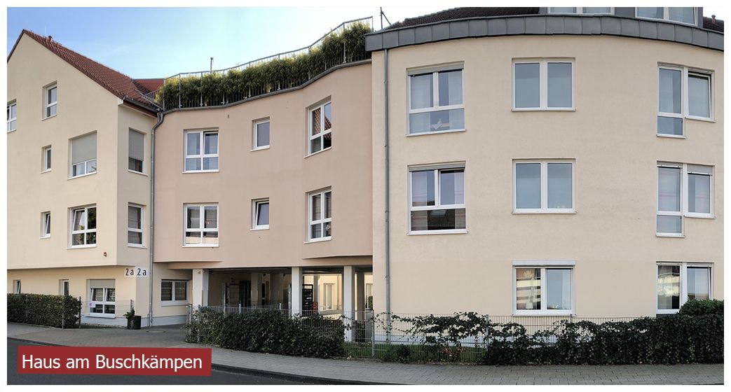 Ein helles, mehrstöckiges Wohn- oder Pflegegebäude mit geschwungener Fassade und grünen Dachbüschen, das als „Buschkampen“ bezeichnet wird.
