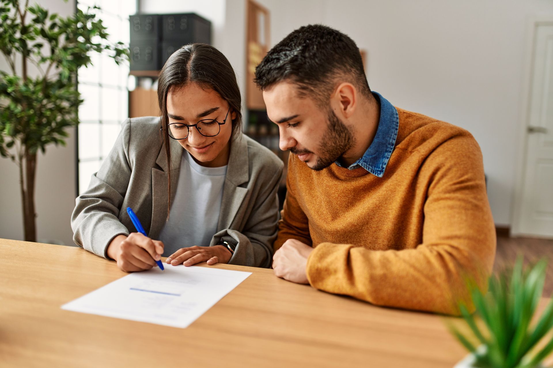 Two coworkers review a document together at a wooden table in a bright office.