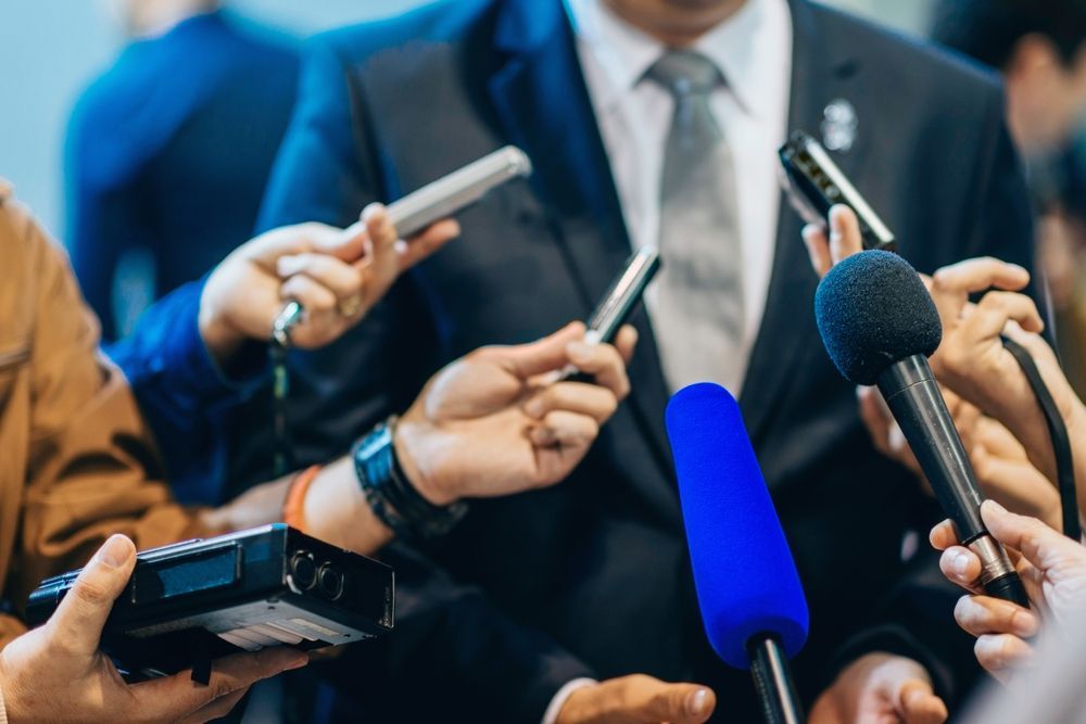 A man in a suit and tie is being interviewed by a group of people holding microphones.
