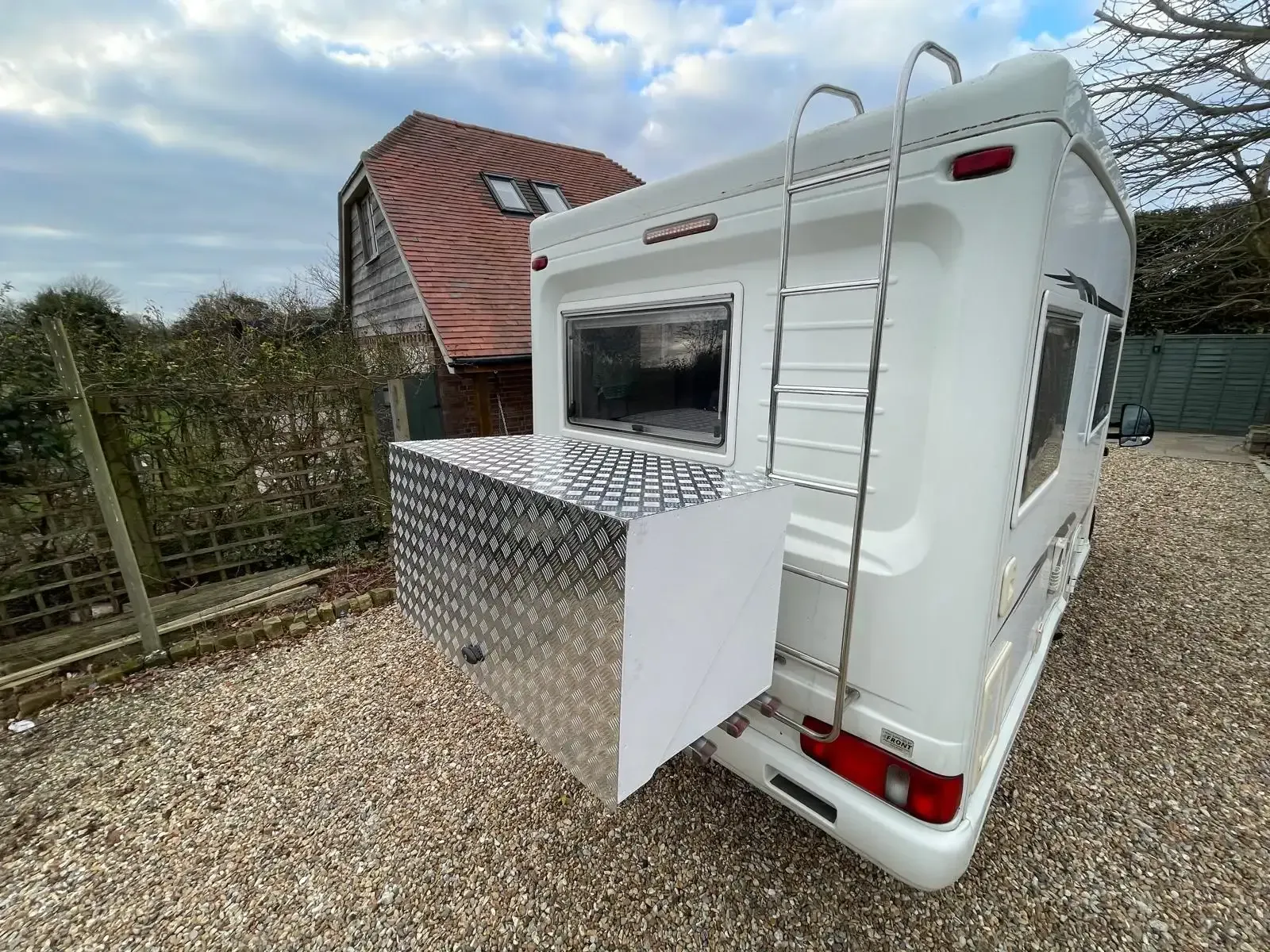 White camper trailer with an aluminum storage box attached to the back. A ladder is mounted on the trailer.