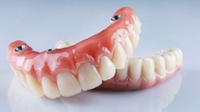 A Pair of Dentures Are Sitting on a Black Surface — Burleigh Heads Denture Clinic Gold Coast in Burleigh Heads, QLD A close up of a full denture on a table. — Burleigh Heads Denture Clinic Gold Coast in Burleigh Heads, QLD