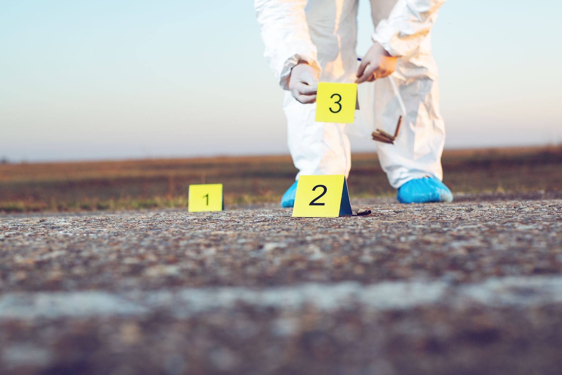 A crime scene investigator in a white suit placing evidence markers on asphalt.