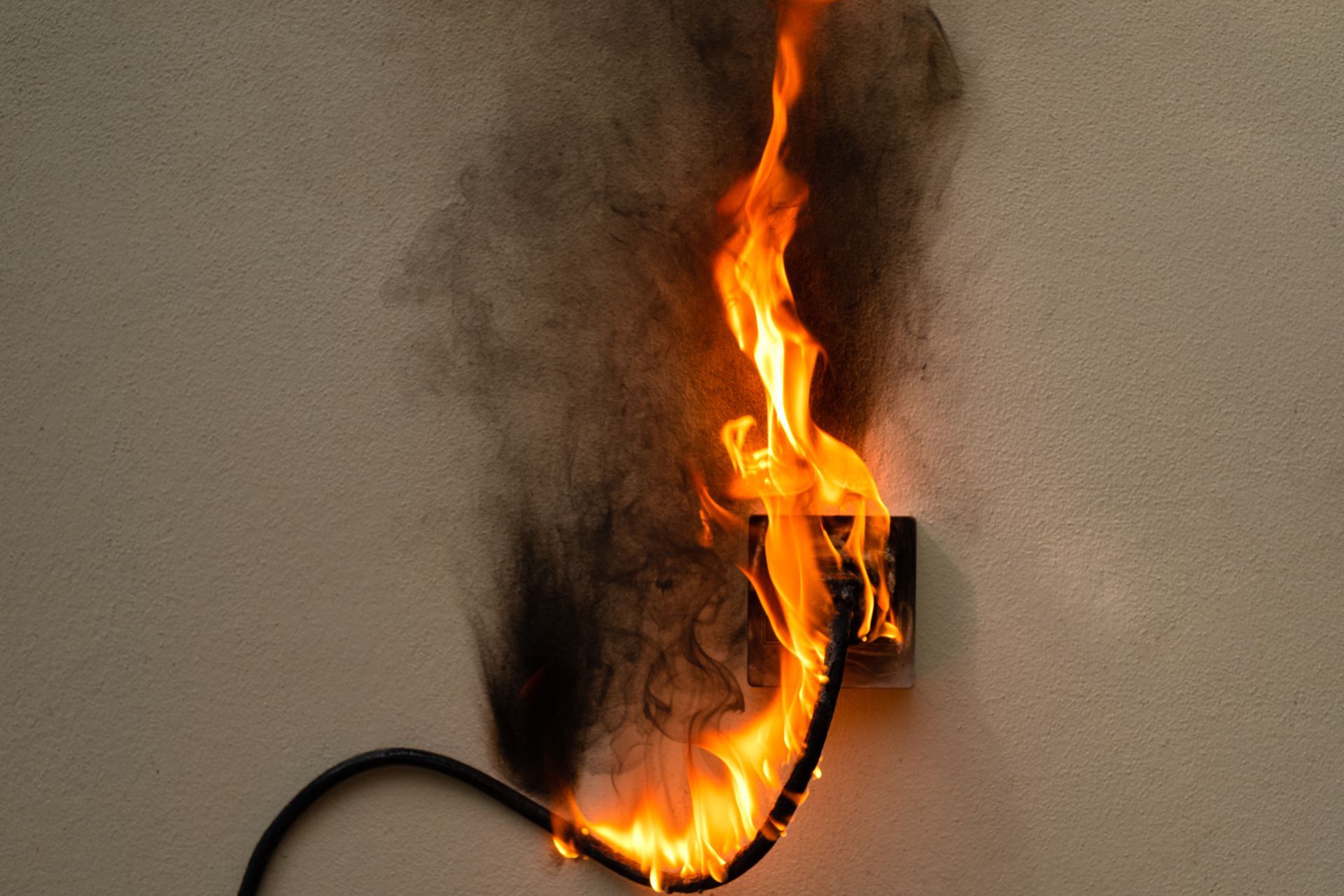 Burning electrical outlet with flames and smoke on a beige wall.