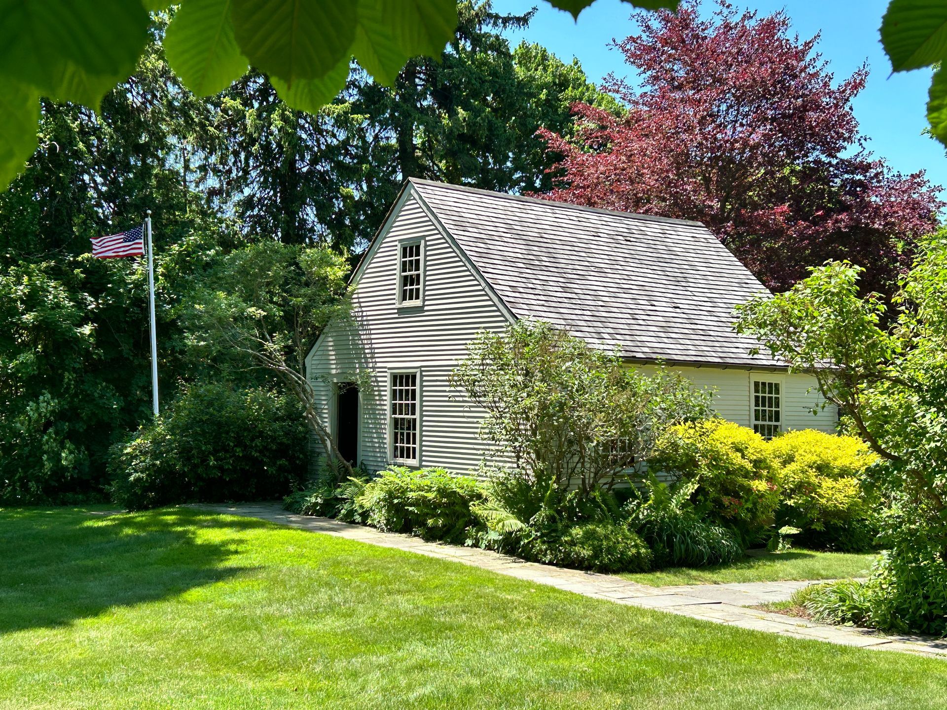 A small white house is surrounded by trees and bushes