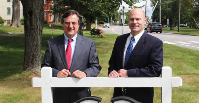 Two men in suits and ties standing next to a white fence