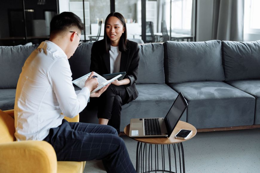 Two people discussing documents on a sofa in a modern living room with a laptop on a coffee table.
