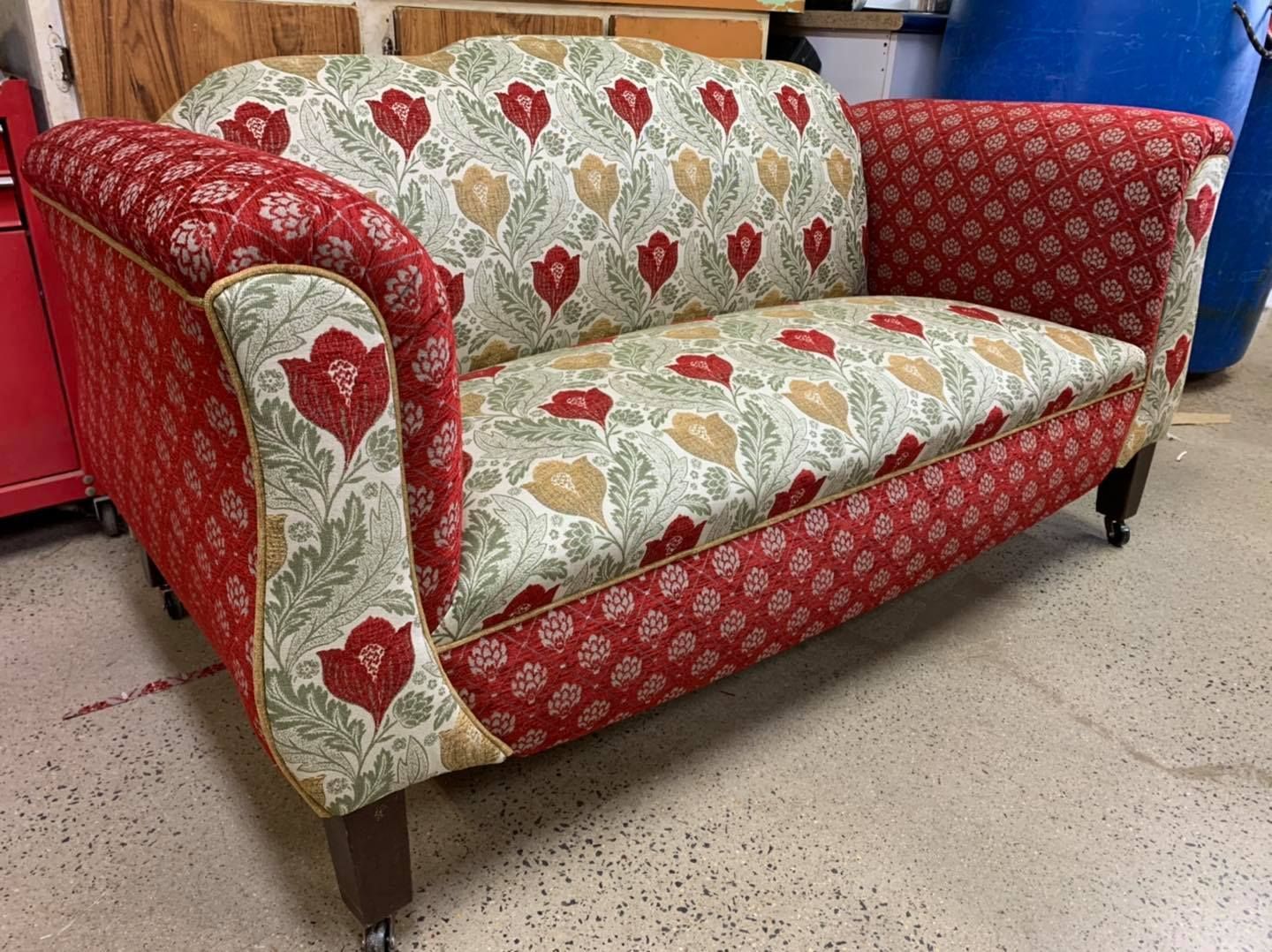 A red and green couch with a floral pattern is sitting on a concrete floor — Aztak Upholstery In Manunda, QLD