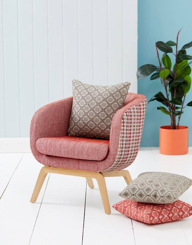 A pink chair with a pillow on it is sitting next to a potted plant.
