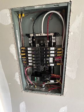 Open electrical breaker panel with exposed wires in a wall recess