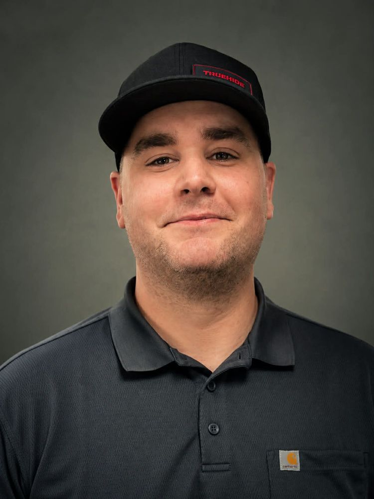 Man wearing a black cap and polo shirt against a plain gray background.