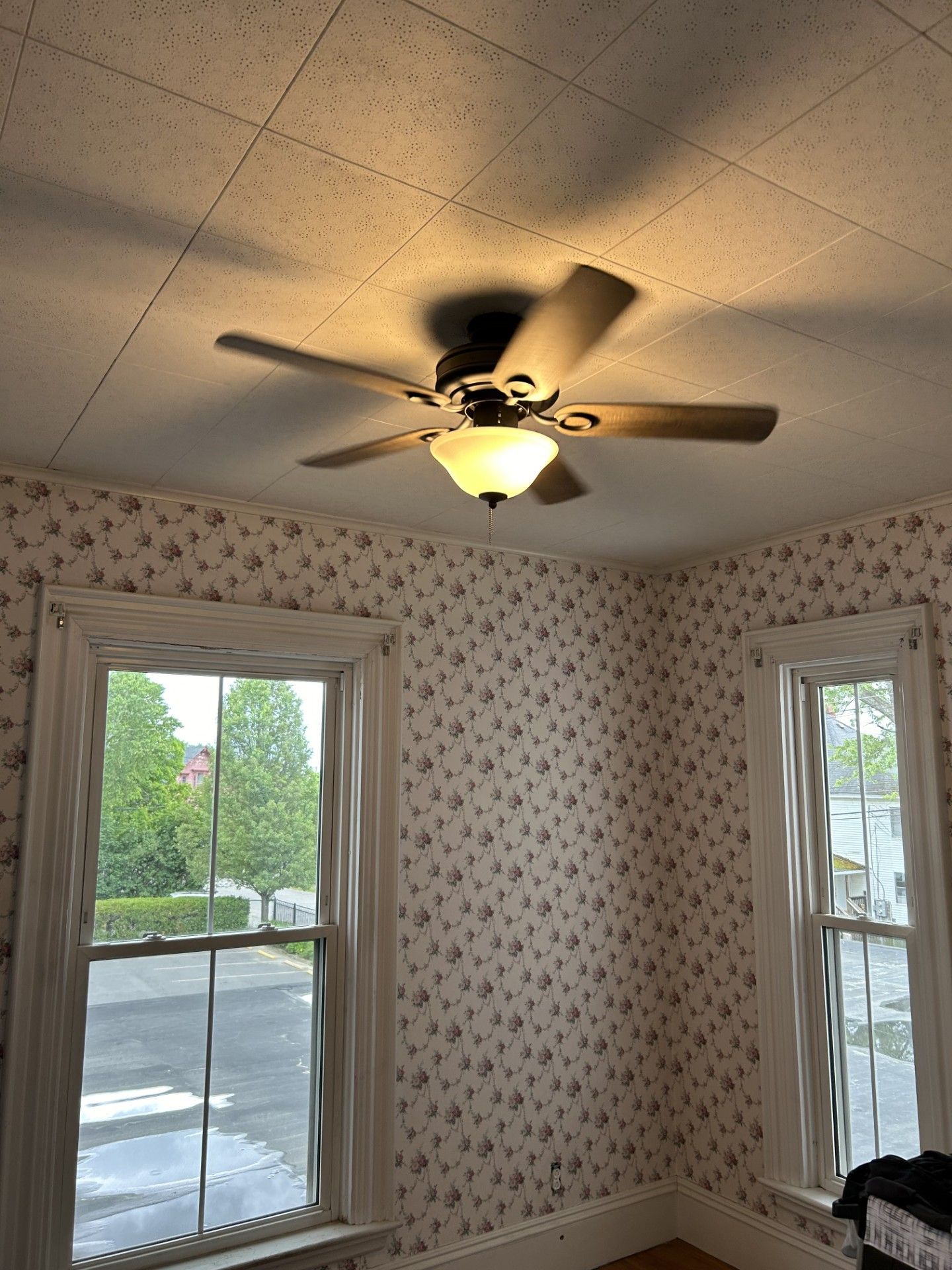 Small room with floral wallpaper, ceiling fan, and two windows overlooking snowy trees.